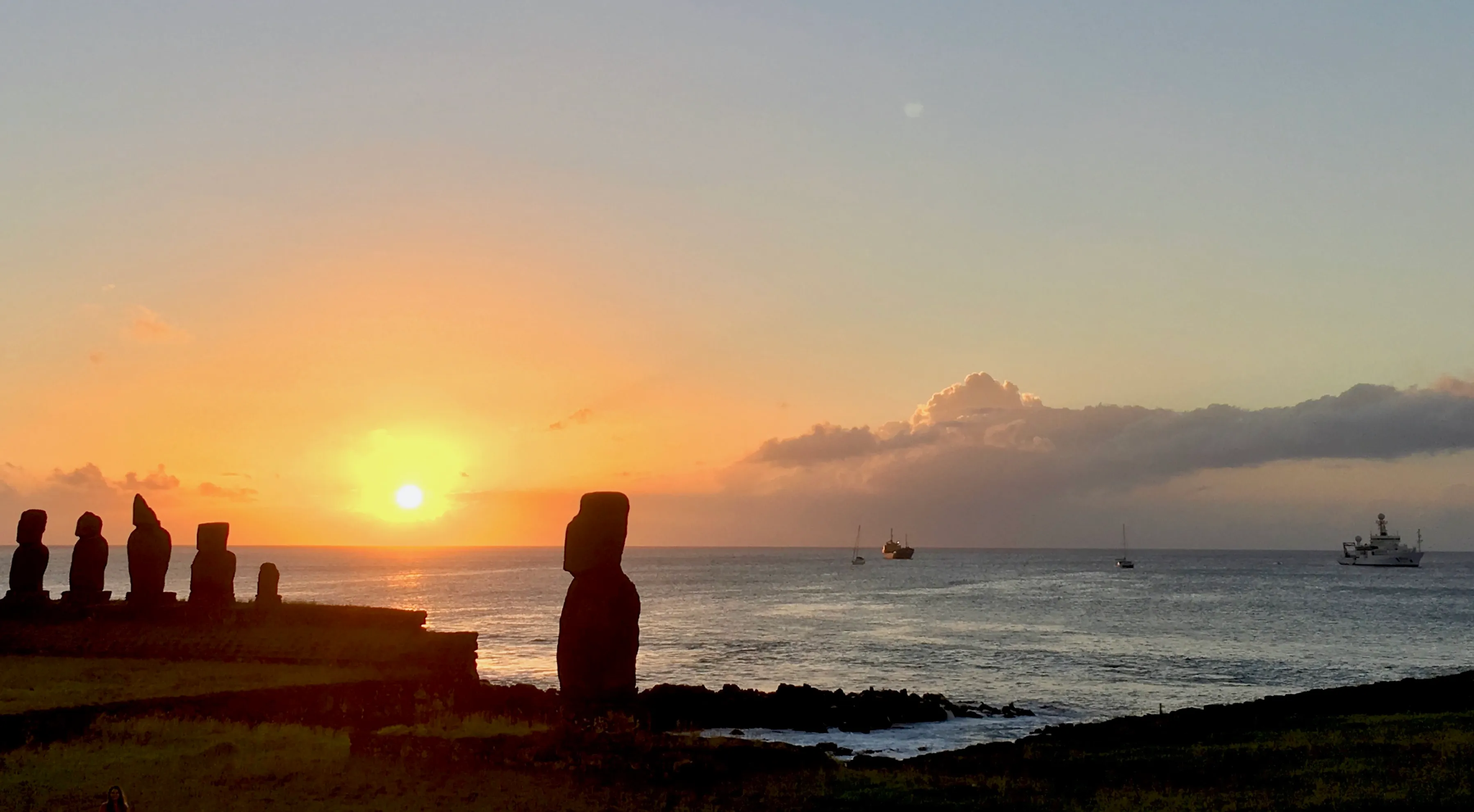 Moai silhouettes at sunset on Rapa Nui with a research ship on the horizon