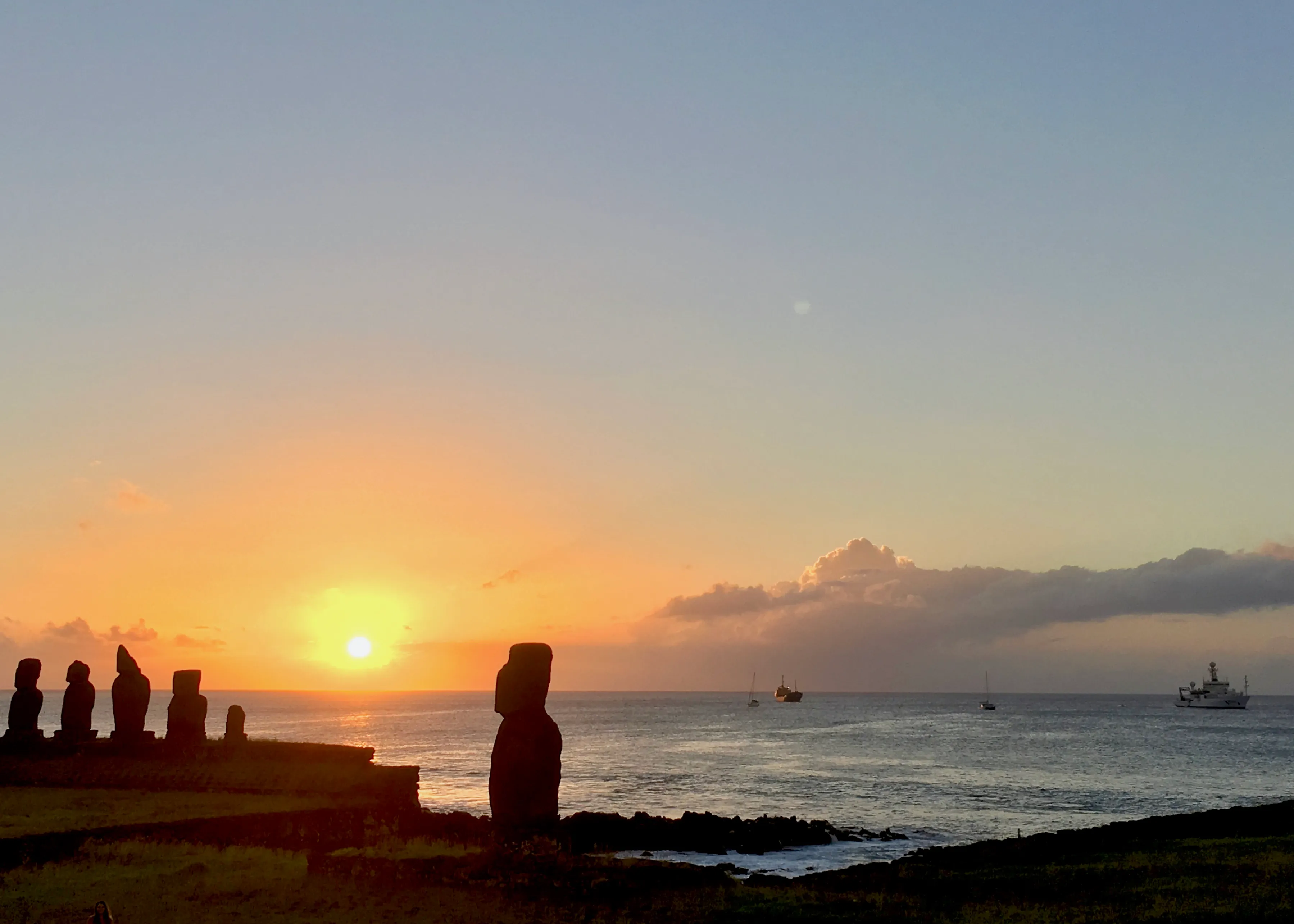 Moai silhouettes at sunset on Rapa Nui with a research ship on the horizon